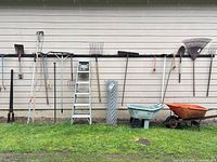 Wide view of tools on rack with ladders, fencing roll, wheelbarrows