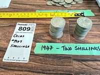 Stacks of 1947 two-shilling coins beside measuring tape and lot tag