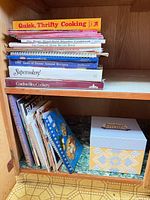 Stack of assorted cookbooks on upper shelf showing titles and formats