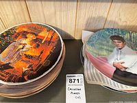 Stack of plates showing Christmas scene plate on top and Elvis plate beneath, lot tag visible