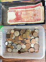 Stack of Greek 100-drachmai notes in metal box above container of mixed coins