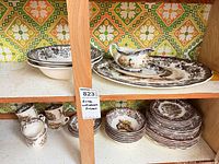 Cabinet shelf with stacked plates, bowls, teacups, gravy boat on platter