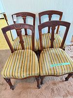 Front view of four matching chairs showing upholstery and carved backs