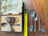 Open case showing sterling egg cup and matching spoon with ruler for scale plus three additional pieces beside