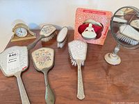 Overview of vanity brushes, pedestal mirror, dresser clock and boxed figurine on tabletop