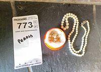 Necklace coiled beside container holding earrings