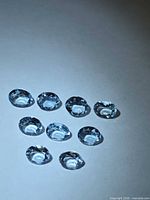 Nine light blue oval-cut aquamarine gemstones on neutral background