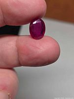 Front view of oval faceted ruby held between fingers