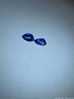 Two pear-cut violet-blue faceted stones on neutral background