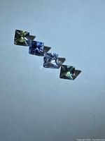 Four square princess-cut multicolored Tanzanites in a row on neutral background