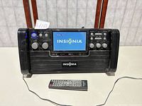 Front view of Insignia portable DVD stereo player with powered-on LCD screen and remote control