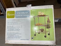 Box front showing assembled chrome 3-tier trolley cart and specifications