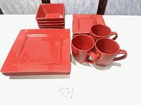 All pieces stacked showing red square plates, bowls and mugs