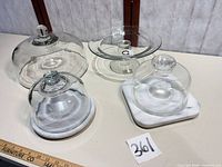 Overview of all four pieces: large glass dome, glass pedestal cake stand, square marble cheese board with dome, round marble board with dome