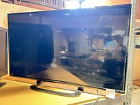 Front view of Sharp 48-inch TV on stand, screen powered showing input label