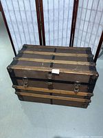 Angled top and front view of trunk showing wood slats, metal bands and hardware