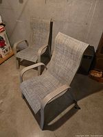 Two metal framed patio chairs side by side on concrete floor