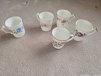 Five Aynsley Chanticlere cups arranged upright showing floral patterns and gold trim