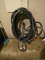 Coiled dark grey garden hose with attached nozzle against wall