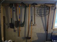 Seven long-handled garden tools hanging on wall