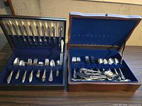 Two wooden presentation boxes open showing stainless steel flatware sets