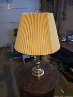 Full view of brass lamp with pleated shade on small table
