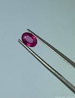 Ruby held in tweezers showing oval faceted cut