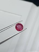 Round ruby held by tweezers showing face-up view