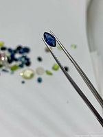 Marquise blue sapphire held by tweezers, other loose stones blurred behind