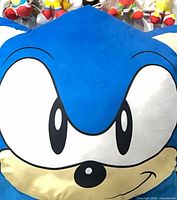 Front view of large Sonic face plush pillow with small plush toys partially visible in background