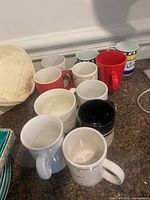 All eleven assorted ceramic mugs grouped on countertop