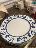 Stack of five matching white plates with blue floral border and green rim