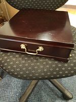 Closed wooden tea box on chair showing top and brass handle