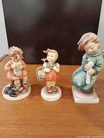 Front view of all three Goebel figurines on wooden surface
