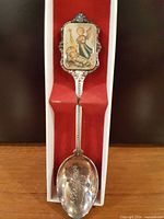 Full spoon in box showing enamel finial and engraved bowl