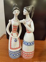 Front view of porcelain figurine showing two women, hand-painted folk patterns