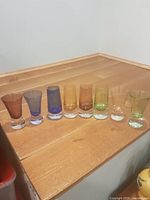 Eight colour-tinted shot glasses lined on wooden surface