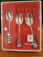 Three ornate silver-plated spoons in red-lined box labeled Justinus Solingen 90 g versilbert