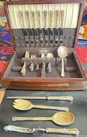 Open chest showing knives, forks, spoons, serving pieces and additional utensils outside chest