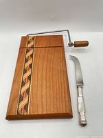 Top view of cheese board with inlay and attached wire slicer beside Birks knife