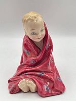 Front view of figurine showing child wrapped in red floral blanket