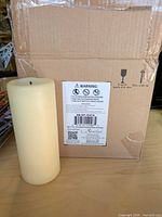 Front view of one ivory pillar candle beside shipping box