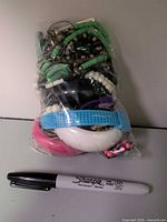 Front view of sealed bag filled with assorted costume jewellery next to marker for scale