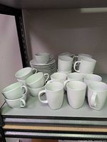 Group of white Apilco cups, saucers and IKEA mugs on shelf