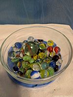 overall lot: clear glass bowl filled with assorted marbles on blue base