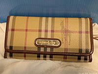 Front view of wallet showing plaid pattern, logo plate, brown trim