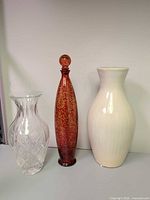 Group shot of red decanter, clear cut glass vase, ivory ceramic vase