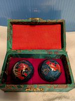 Baoding balls seated in open brocade box showing red interior and clasp