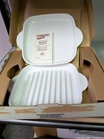 Open box showing flat dish on top of ridged grill pan with instruction booklet