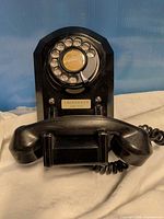 Front view of black wall-mount rotary telephone showing dial and emergency label